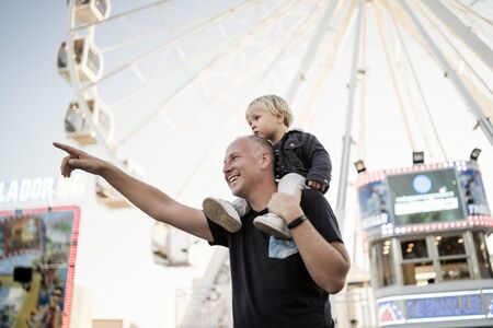 Happy father with his little piggybacked son in an amusement park