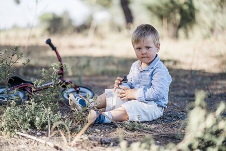 Cute toddler drinking water from the bidon next to bicycle in the natureの写真素材