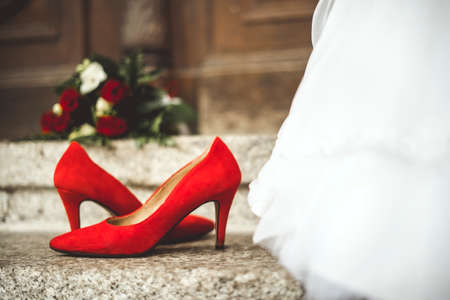 Red shoes and bouquet next to wedding dress of brideの写真素材