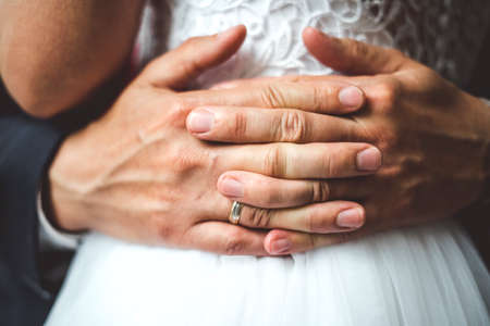 Close up of groom's palms with wedding ring embracing bride.の写真素材