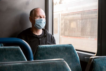 Serious man wearing surgical mask looking through the window in a train