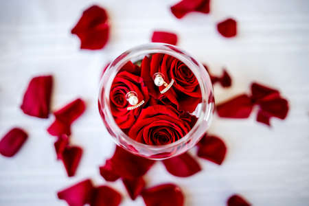 Romantic elegant earring in the glass with roses and rose petals aroundの写真素材