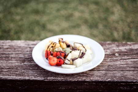 Delicious fruit salad with chocolate topping on wooden benchの写真素材