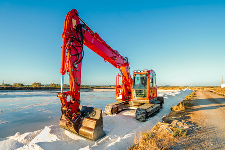 Red bulldozer harvesting sea salt from pond and making a heap of salt at salines in Faro, Algarve,...