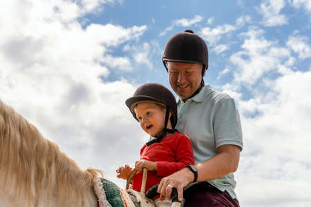 Father and son enjoying horse riding in the paddockの写真素材