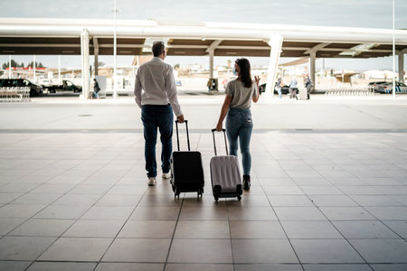 A couple of friends with luggage wearing protective masks  leaving the airportの写真素材