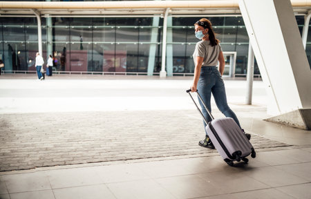 A young woman wearing mask walking with the luggage to the airportの写真素材