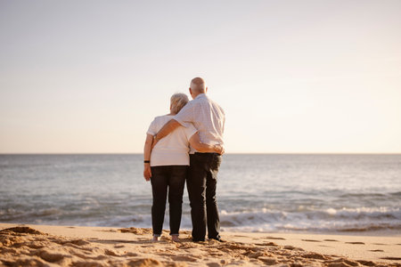 Elderly couple hugging each other on the beach seen from their backの写真素材