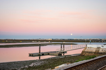 Morning view of pier on Ria Formosa in Faro, with moon set shortly before sun rise, Algarve, southern Portugalの写真素材
