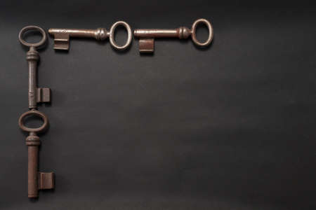Four old, slightly rusty tumbler keys arranged as a frame on a black background