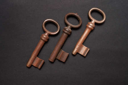 Group of three old and slightly rusted tumbler keys on a black background. The arrangement is...