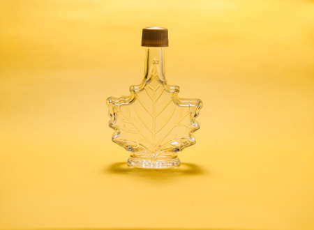Empty bottle in the shape of a maple leaf against a yellow backgroundの写真素材