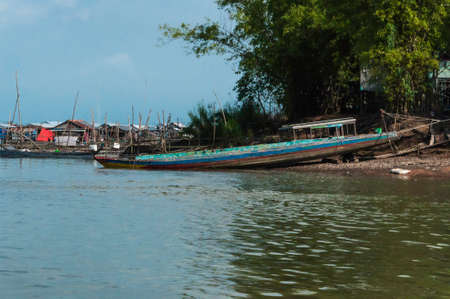 Traditional wooden fishing boat in Asia, it is partly on dry land, in the background a fishing villageの写真素材