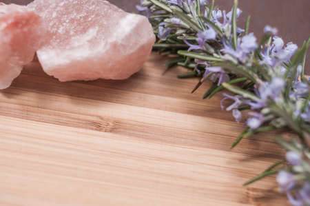 Flowering rosemary placed between large pink salt stones, positioned on a bamboo boardの写真素材