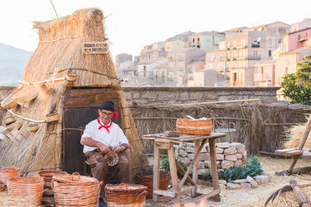August 18, 2017 - Gangi, Sicily Italy. Man builds a wicker basket with traditional Sicilian clothes. Representation of a camp used during wheat harvest.のeditorial素材
