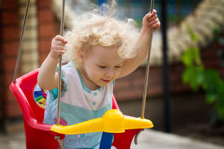 Adorable blonde curly hair little girl having fun on a swing