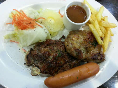Close up photo of mix pork and chicken steak serve with potato chips and salad on white plate.の素材