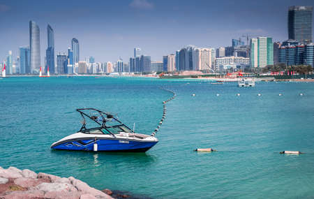 Febuary 1, 2018: Samll Blue yacht docked at Marina Abu Dhabi, against Abu Dhabi Iconic buildings, United Arab Emiratesのeditorial素材