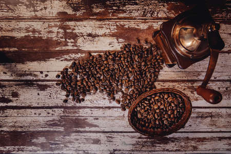 top elevated view of roasted coffee beans in a basket next to an antique metal and wood hand coffee grinder on a wooden tableの写真素材