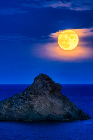 yellow super full moon in blue hour over the sea and mountainsの写真素材