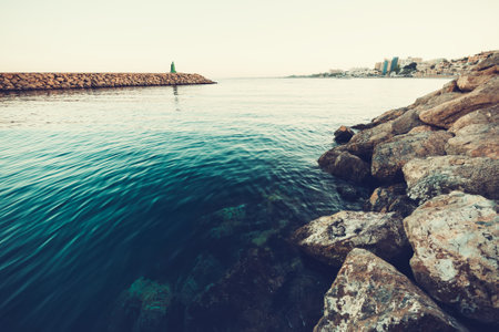 lighthouse with the city in front and the sea and rocks in the foregroundの写真素材