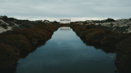 water inlet channel to the salt flats with an old building in the center of itの写真素材