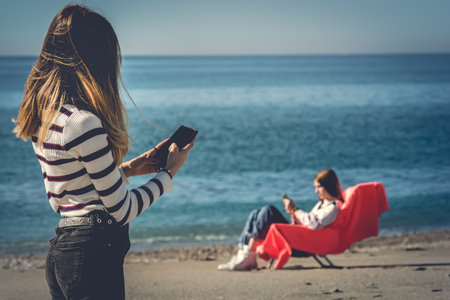 Young couple sitting on the beach and taking a selfie with mobile phoneの写真素材