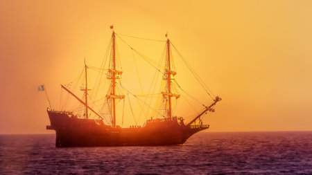 Silhouette of pirate ship sailing at sunset backlit by sunlightの写真素材