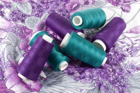 Bobbins of green and purple threads on piece of cloth with pattern