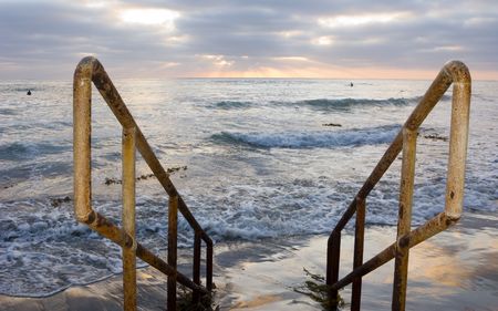 Rusty Yellow Handrails and Sunset Surfers in Ocean Wavesの写真素材