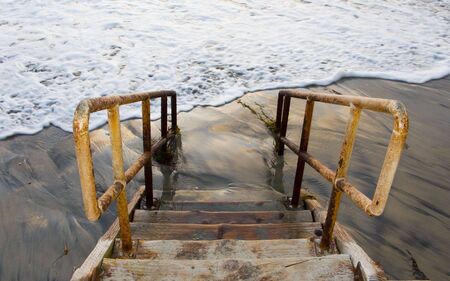 Rusty Yellow Handrails and Beach Stairs to Water and Sandの写真素材