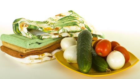 Fresh cucumbers, tomatoes, onions on plate with kitchen towelsの写真素材