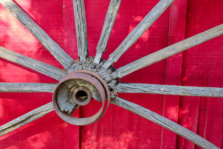 Wooden spokes and hub with rusty iron rings of old cart wheel on red wall backgroundの写真素材