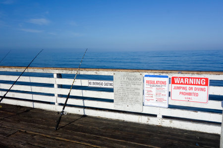 Fishing Rods and warnings about food poisoning and city regulations around beaches, cliffs, walkways and parking areas posted at Crystal Pier, San Diego, Californiaの写真素材
