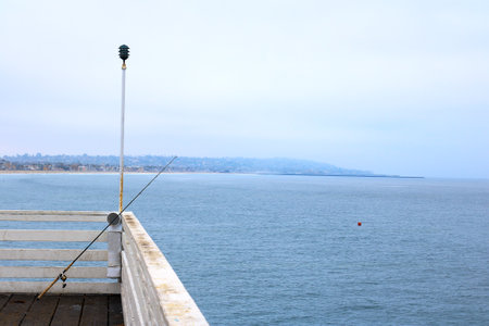 Black fishing rod mounted on Crystal pier barrier and distant sands of Pacific beach in San Diego, Californiaの写真素材