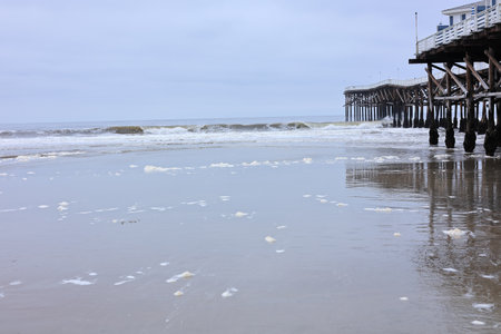 Breezy cool morning and relaxing waves rolling over sandy shore of Pacific beach near historic wooden Crystal pier, San Diego, CAの写真素材