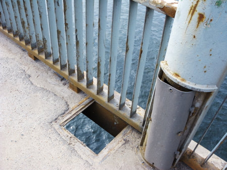 Open square manhole in a bridge overpass over river waters next to run down electric wiring box