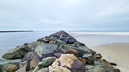 Narrow strip of green and brown rocks stretching into Pacific ocean at Point Medanos Jetty separating South Mission beach from entrance channel to the bay area, San Diego, Californiaの写真素材