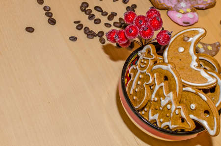 Christmas gingerbreads with white frosting in a colorful bowl, coffee beans and rowan twig for decoration on a wooden boardの写真素材