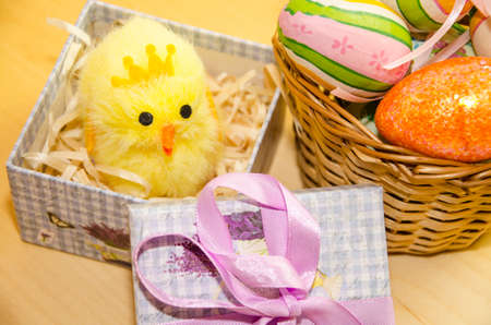 Colorful Easter eggs in the basket and a yellow chicken in a gift box