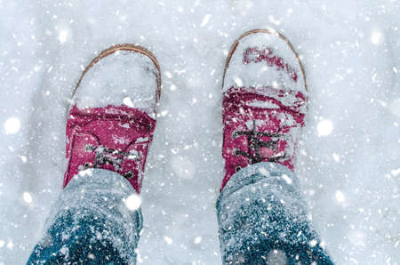 Close up of legs in blue jeans and pink hiking boots covered with snowの写真素材