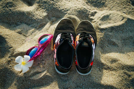 Sneakers with sunglasses and frangipani flower on the beach sandの写真素材
