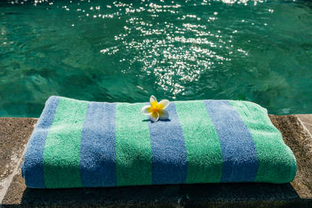 Blue towel and franjipani flower near swimming pool