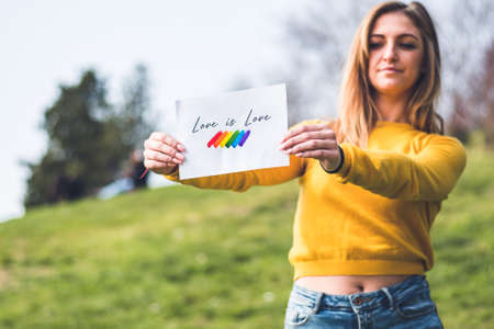 woman holding sign with the slogan love is love and the flag with the LGTBIQ colors red, orange, yellow, green, blue and purpleの写真素材