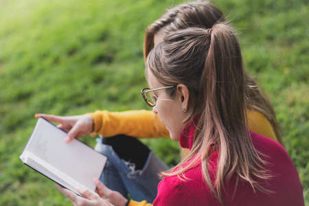 Two women enjoying reading an interesting book in an outdoor park