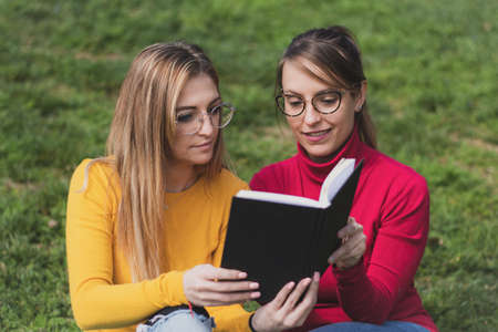 Two women enjoying reading an interesting book in an outdoor parkの写真素材