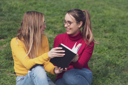 Two women enjoying reading an interesting book in an outdoor park