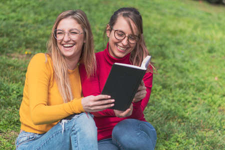 Two women enjoying reading an interesting book in an outdoor park