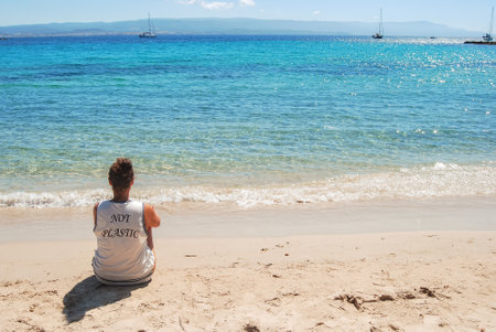 Woman sitting on the beach looking at the sea with message on the t-shirt Not plasticsの写真素材