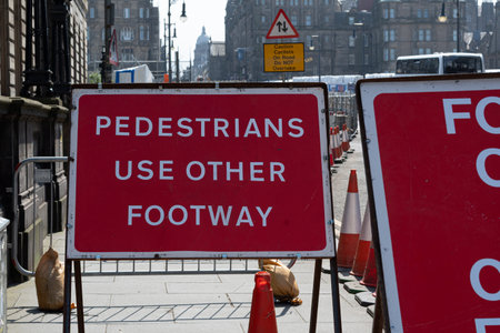 Red sign advising pedestrians to use other footway during roadworks in edinburgh city centerの写真素材